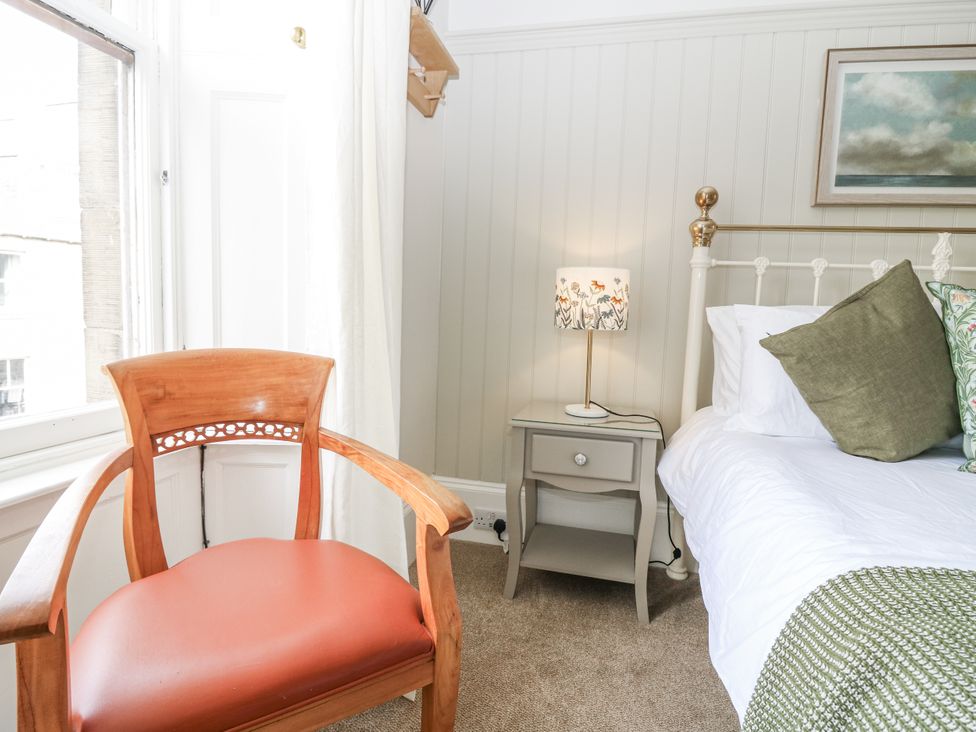 A bedroom with a bed, nightstand, lamp, and chair at 11A High Street in Jedburgh