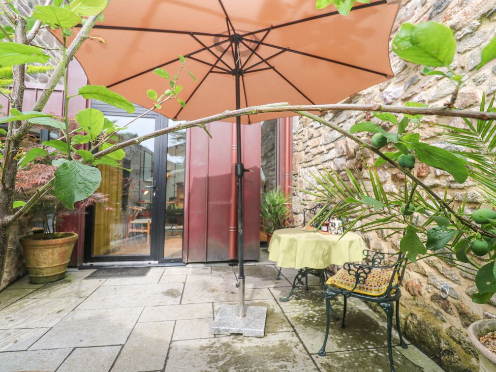 An outdoor area with a table and chair under an umbrella at The Stables in St Just