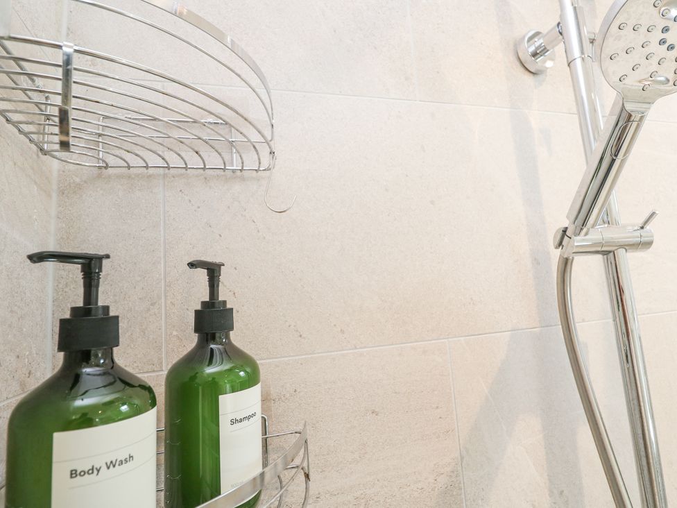 A shower area with a shelf and containers for body wash and shampoo at The Stables St Just