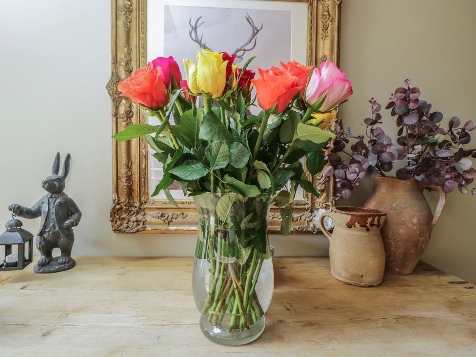 A bouquet of roses in a vase with a rabbit statue and ceramic pot at Cotswold House Moreton-In-Marsh