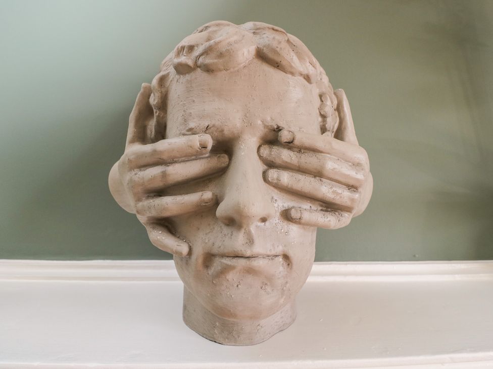 A sculpture of a face with hands covering the eyes at Cotswold House in Moreton-In-Marsh