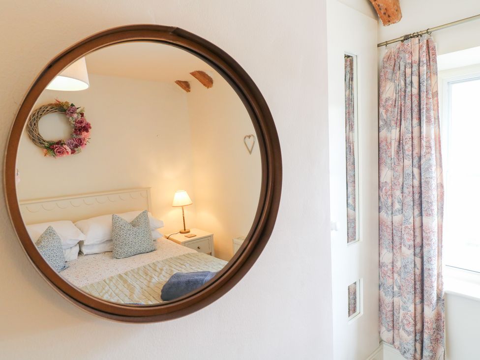 A bedroom with a mirror reflecting a bed and lamp at Rose Cottage in Hartington
