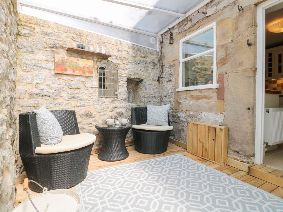 A conservatory with stone walls, two chairs and a small table at Rose Cottage in Hartington