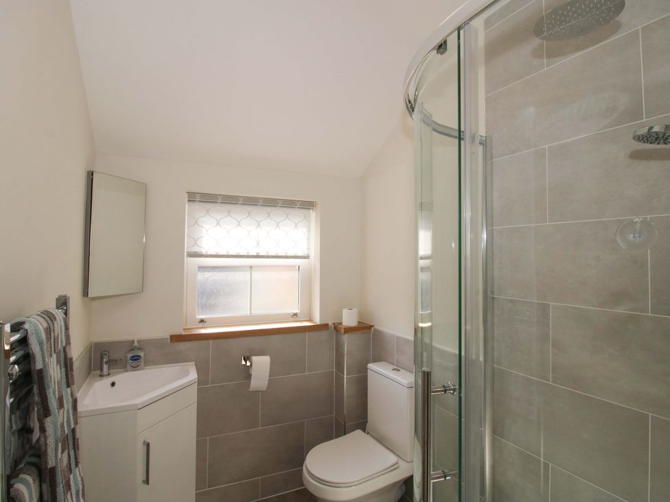 A bathroom with a shower, toilet, sink, and mirror at Riverside Cottage in Shrewsbury