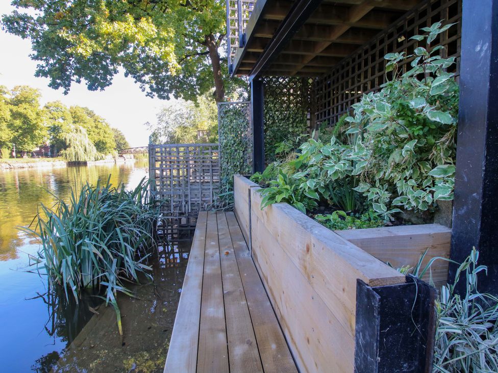 A wooden deck with planters beside a river at Riverside Cottage in Shrewsbury