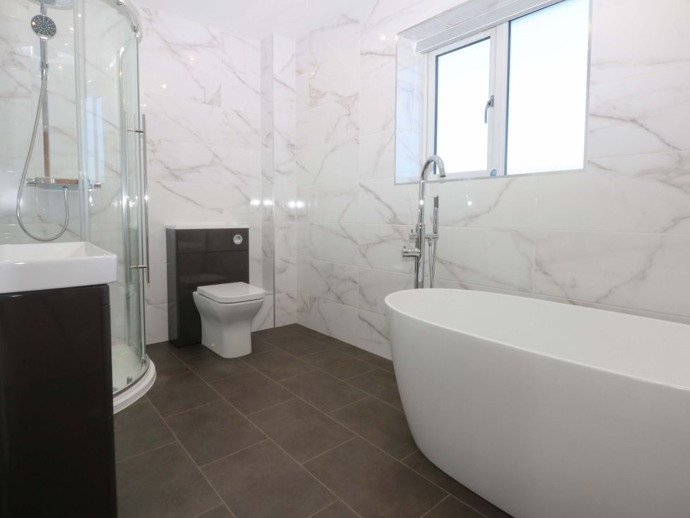 A bathroom with a shower, bathtub, and toilet at 15 Llys Tegeirian in Llangristiolus near Llangefni