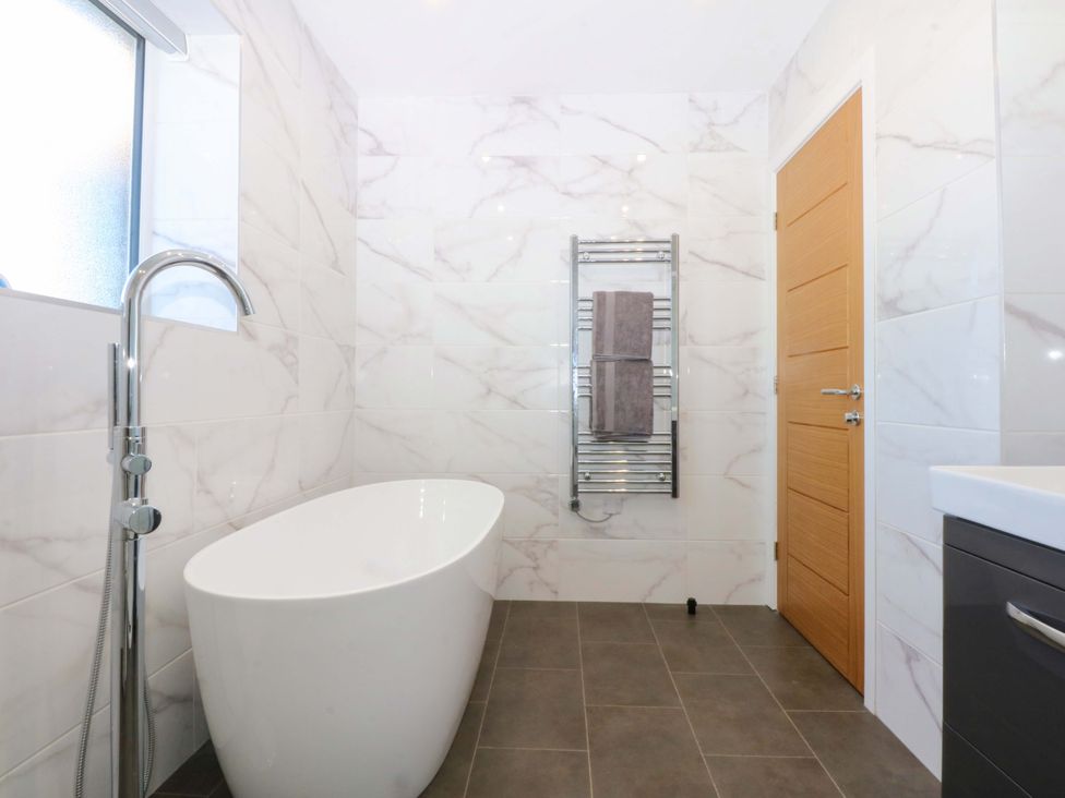 A bathroom with a bathtub, towel rail and sink at 15 Llys Tegeirian in Llangristiolus near Llangefni