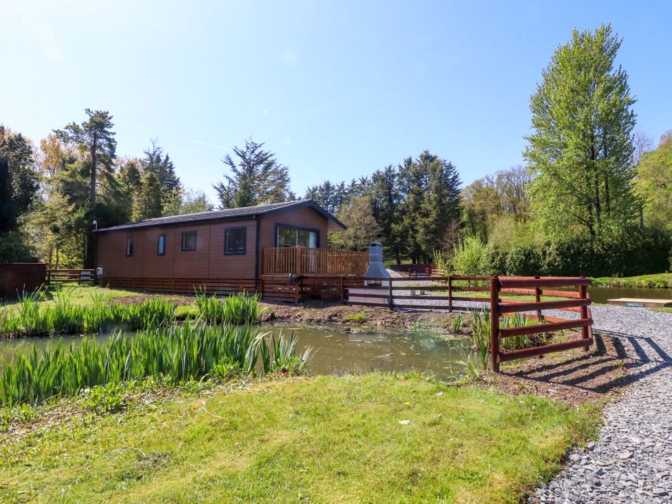 A cabin with a deck next to a pond at Lakeview Lodge in Forton near Garstang