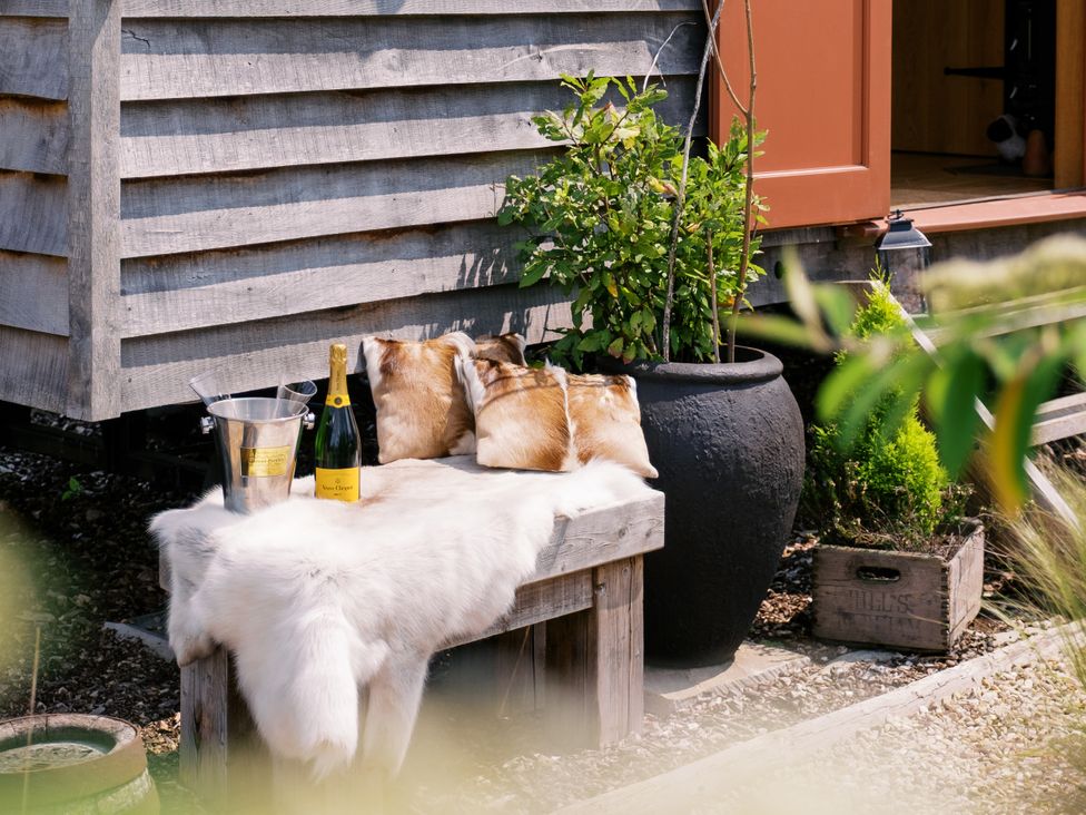 An outdoor seating area with a wooden bench and champagne at Bonnie's Shepherds Hut at Shepherds Lodge Retreat and Wellness Bottesford near Redmile and Vale of Belvoir