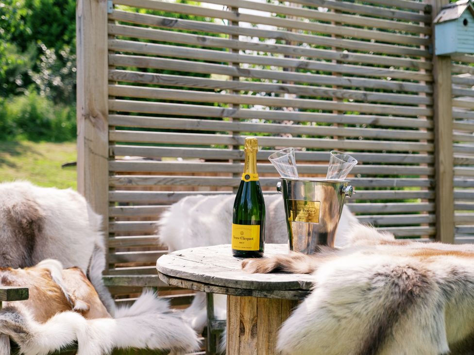 An outdoor seating area with a bottle of champagne and flutes at Bonnie's Shepherds Hut at Shepherds Lodge Retreat and Wellness near Bottesford