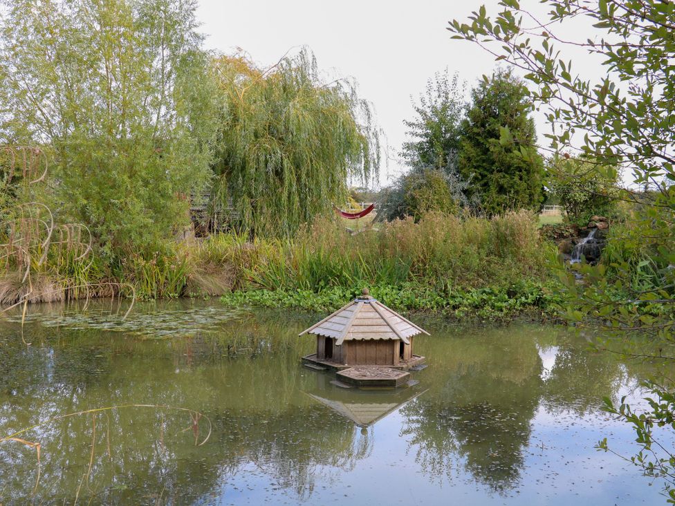 A pond with a wooden hut and trees at Lillie's Shepherds Hut at Shepherds Lodge Retreat and Wellness Bottesford near Redmile and Vale of Belvoir