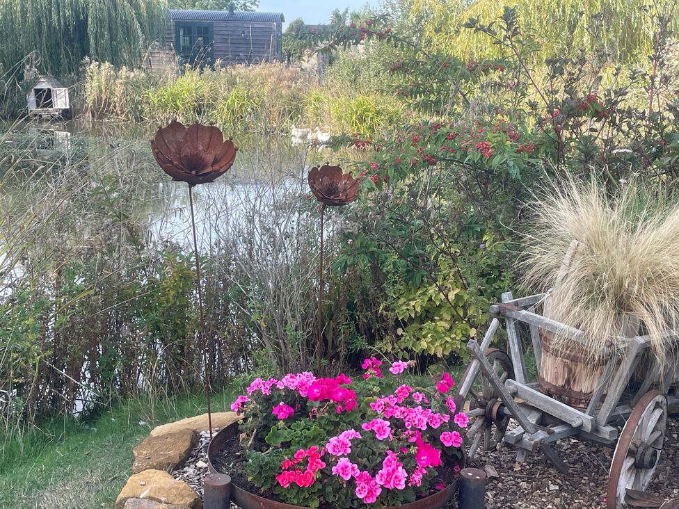 A garden with flowers and metal sculptures near a water body at Lillie's Shepherds Hut at Shepherds Lodge Retreat and Wellness Bottesford near Redmile and Vale of Belvoir