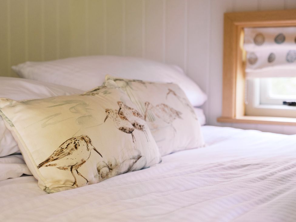 A bed with patterned pillows and a window at Herbie's Shepherds Hut at Shepherds Lodge Retreat and Wellness Bottesford near Redmile and Vale of Belvoir