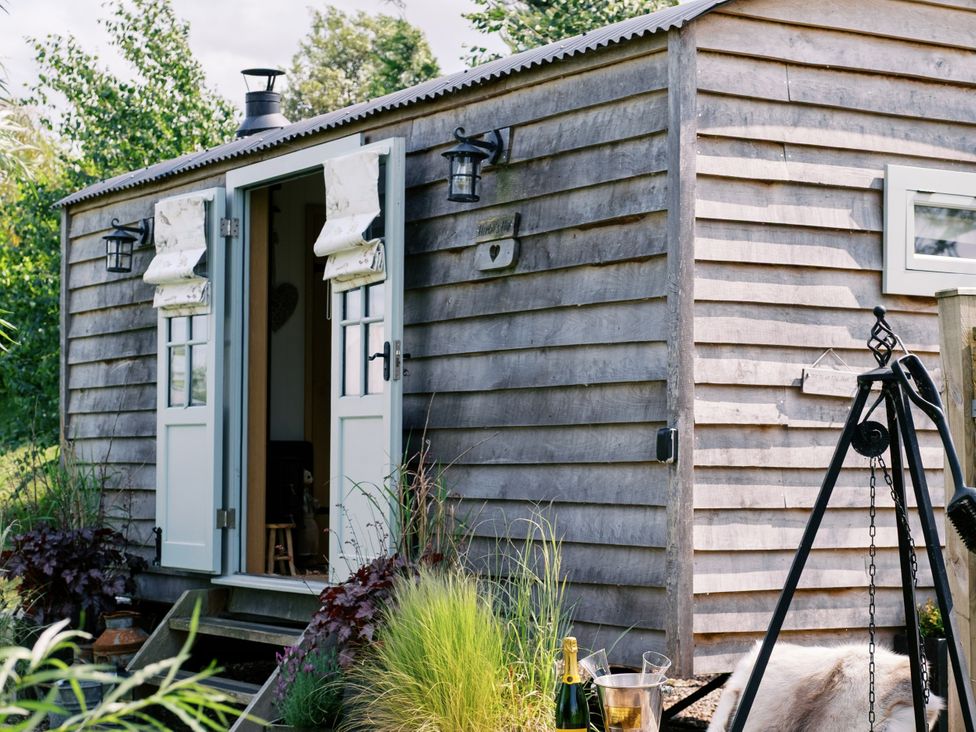 An outdoor view of a wooden cabin with double doors at Herbie's Shepherds Hut at Shepherds Lodge Retreat and Wellness, Bottesford near Redmile and Vale of Belvoir