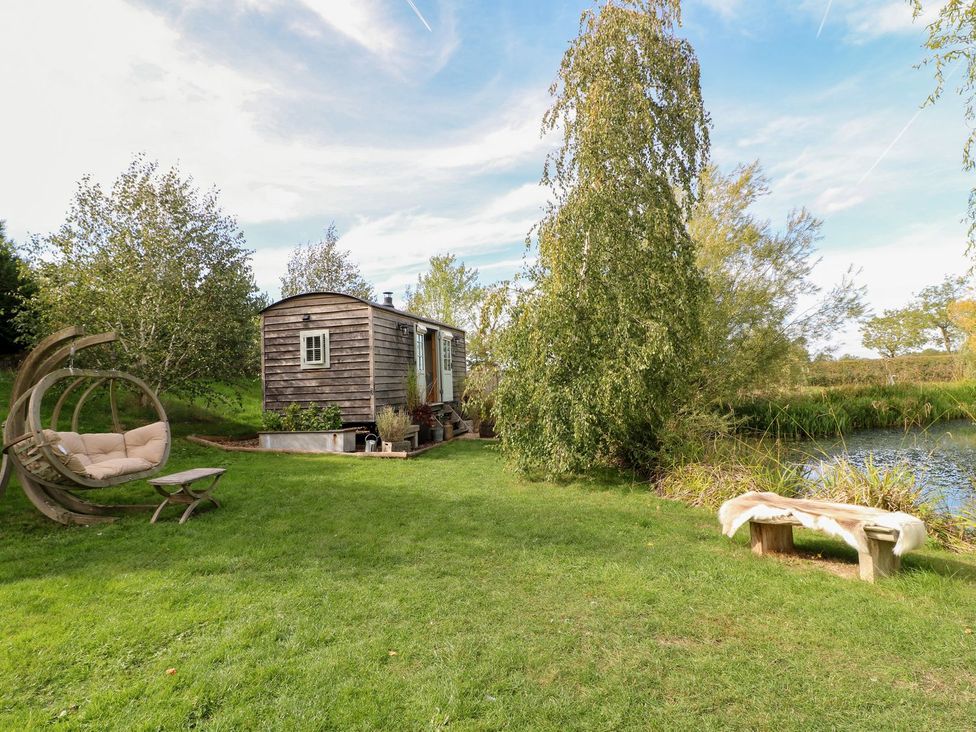 A wooden hut and seating area beside a pond at Herbie's Shepherds Hut at Shepherds Lodge Retreat and Wellness Bottesford near Redmile and Vale of Belvoir