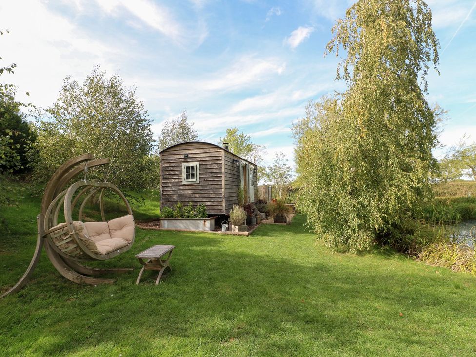 A shepherd's hut with a hanging chair and a table at Herbie's Shepherds Hut at Shepherds Lodge Retreat and Wellness Bottesford near Redmile and Vale of Belvoir