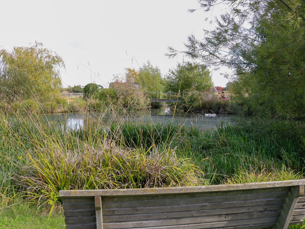 A view of a pond with a bench and surrounding trees at Herbie's Shepherds Hut at Shepherds Lodge Retreat and Wellness in Bottesford near Redmile and Vale of Belvoir