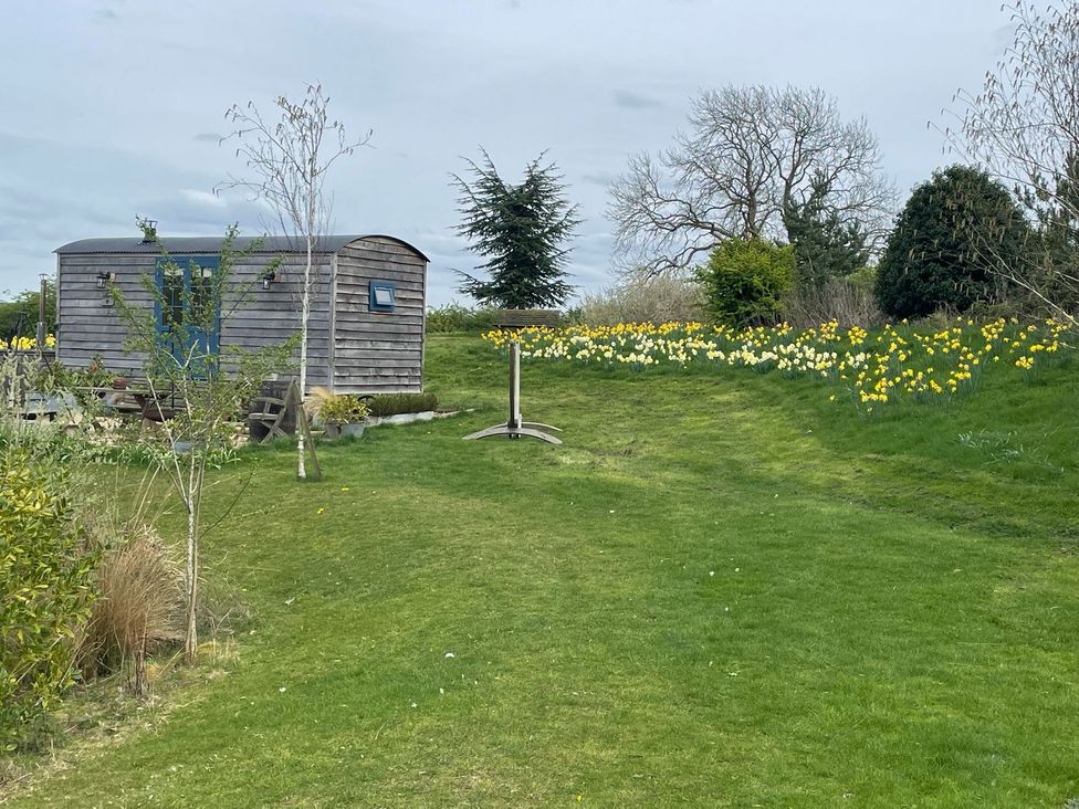 A wooden hut in a garden with flowers and trees at Herbie's Shepherds Hut at Shepherds Lodge Retreat and Wellness, Bottesford near Redmile and Vale of Belvoir