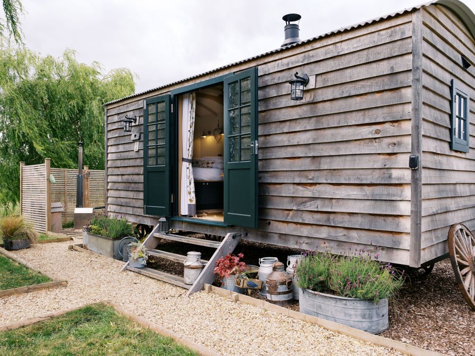 An outdoor view of a wooden hut with green doors and gravel path at Poppie's Shepherds Hut at Shepherds Lodge Retreat and Wellness Bottesford near Redmile and Vale of Belvoir