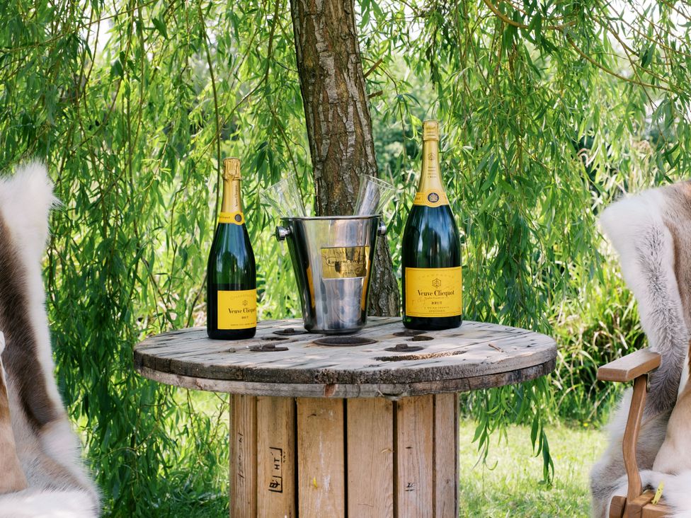 A wooden table with champagne bottles and an ice bucket surrounded by trees at Poppie's Shepherds Hut at Shepherds Lodge Retreat and Wellness in Bottesford near Redmile and Vale of Belvoir