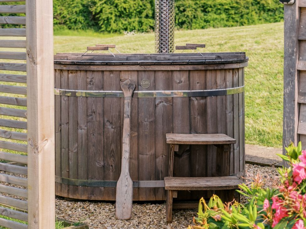 A wooden hot tub with a paddle and steps in a garden at Poppie's Shepherds Hut at Shepherds Lodge Retreat and Wellness Bottesford near Redmile and Vale of Belvoir