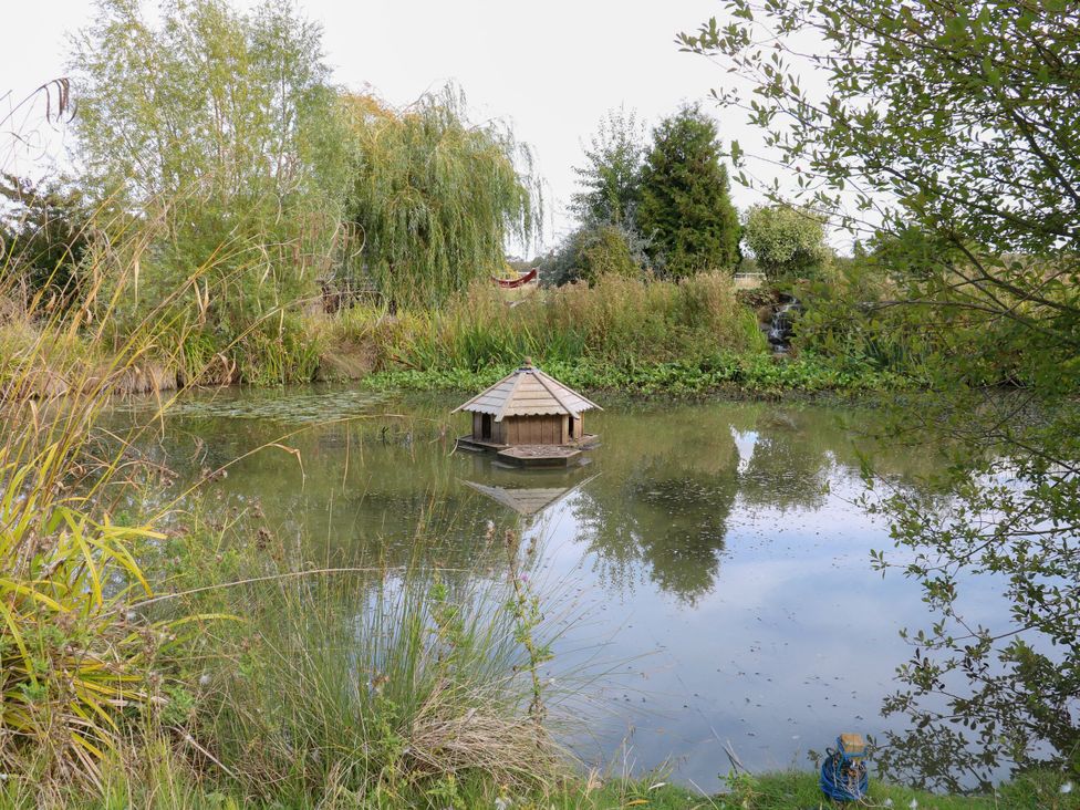 A pond with an island structure surrounded by vegetation at Poppie's Shepherds Hut at Shepherds Lodge Retreat and Wellness Bottesford near Redmile and Vale of Belvoir