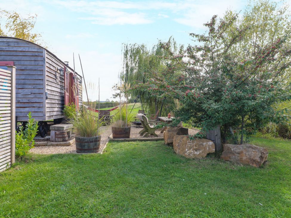 A wooden hut surrounded by plants and rocks at Poppie's Shepherds Hut at Shepherds Lodge Retreat and Wellness, Bottesford near Redmile and Vale of Belvoir