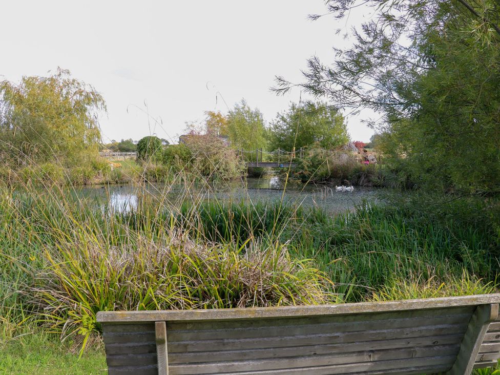 A bench beside a pond with a bridge and trees at Poppie's Shepherds Hut at Shepherds Lodge Retreat and Wellness Bottesford near Redmile and Vale of Belvoir
