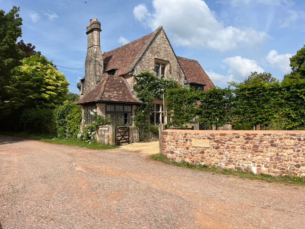 A stone house with a tiled roof surrounded by greenery and a stone wall with a sign that reads The Gables in Spaxton near Nether Stowey