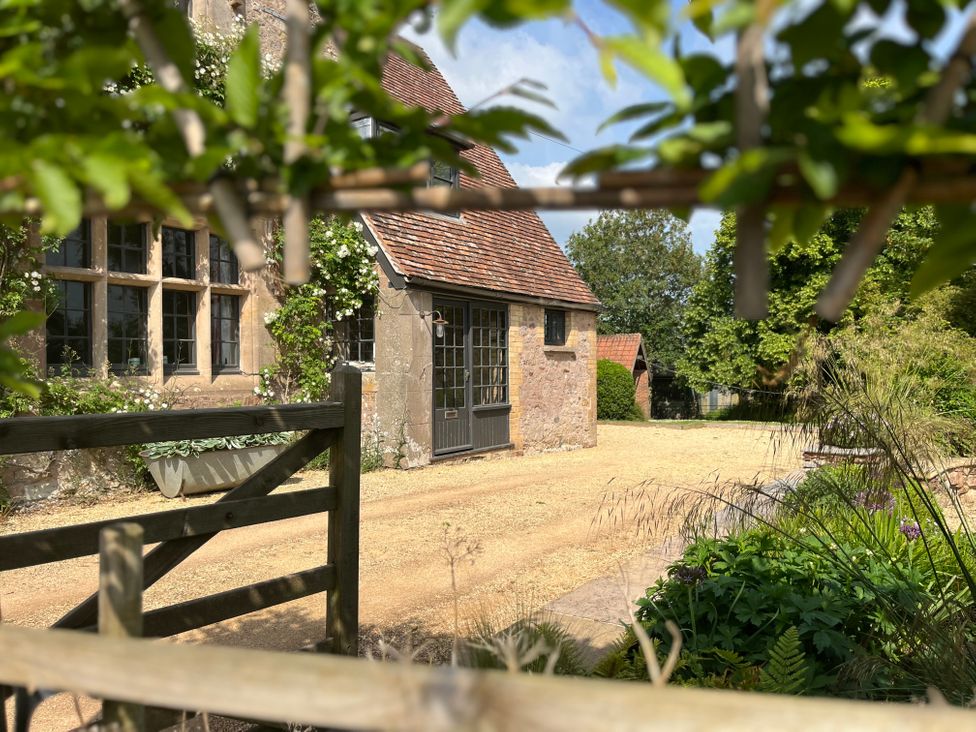 A stone house with tiled roof and windows surrounded by gravel driveway and greenery at The Gables in Spaxton near Nether Stowey