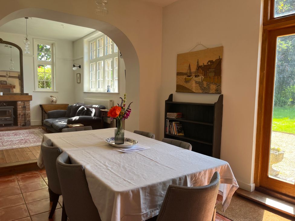 A dining area with table and chairs next to a bookshelf and large windows overlooking the garden at The Gables in Spaxton near Nether Stowey