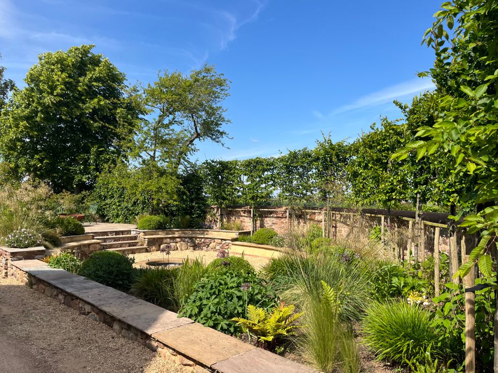 A garden with stone walls and benches surrounded by various plants and trees at The Gables in Spaxton near Nether Stowey