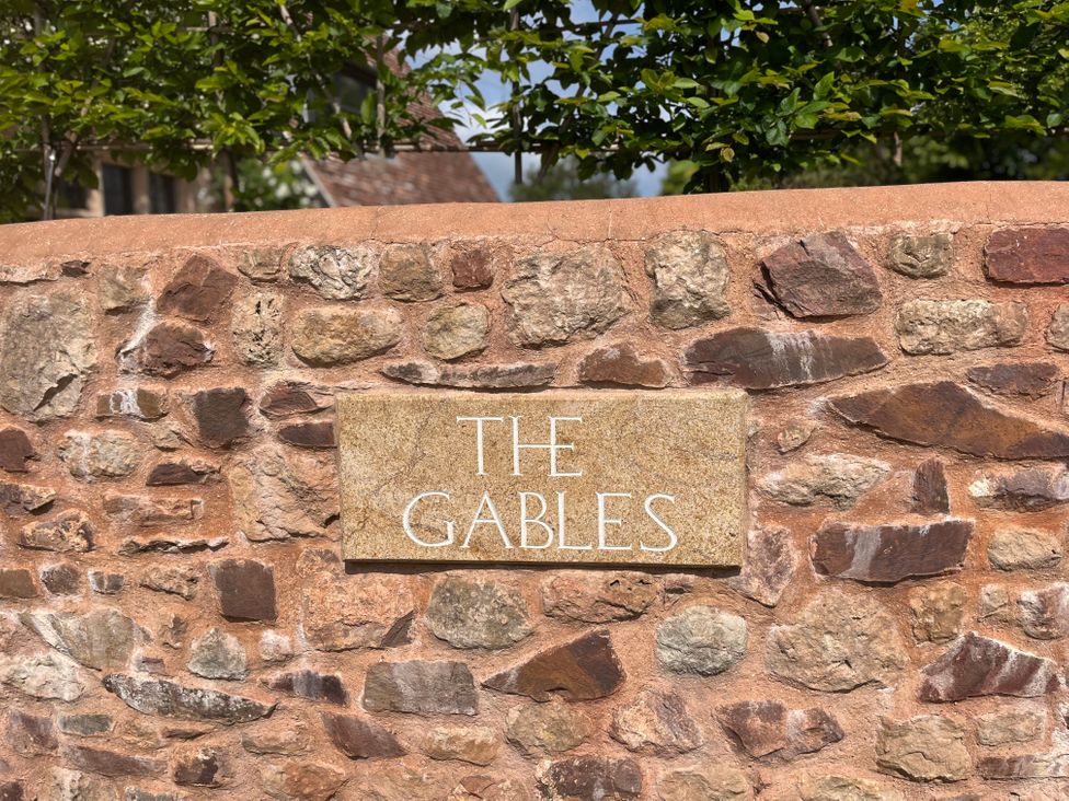 A stone wall with a sign that reads The Gables surrounded by greenery at The Gables in Spaxton near Nether Stowey