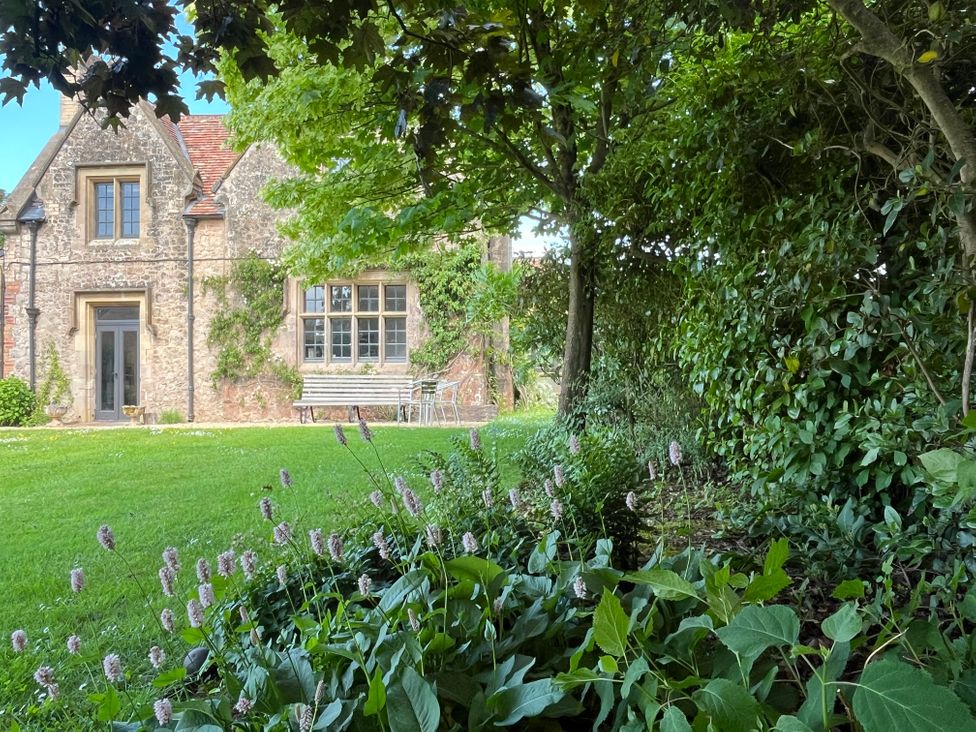 A garden with flowers and trees in front of a stone house at The Gables in Spaxton near Nether Stowey