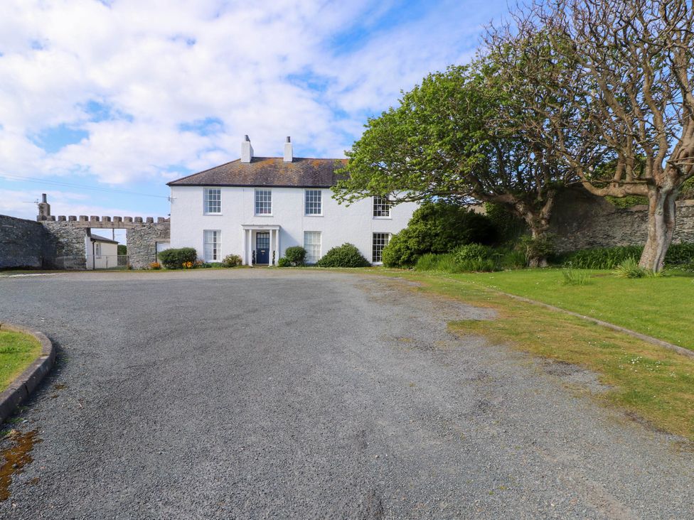 A white two-story house with a gravel driveway green grass and trees at Flat 3 Trearddur Bay