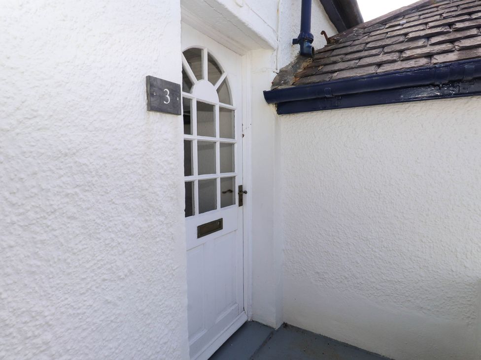 An exterior white door with glass panels and a mailbox slot next to a pebbledash wall with number 3 on a plaque at Flat 3 in Trearddur Bay