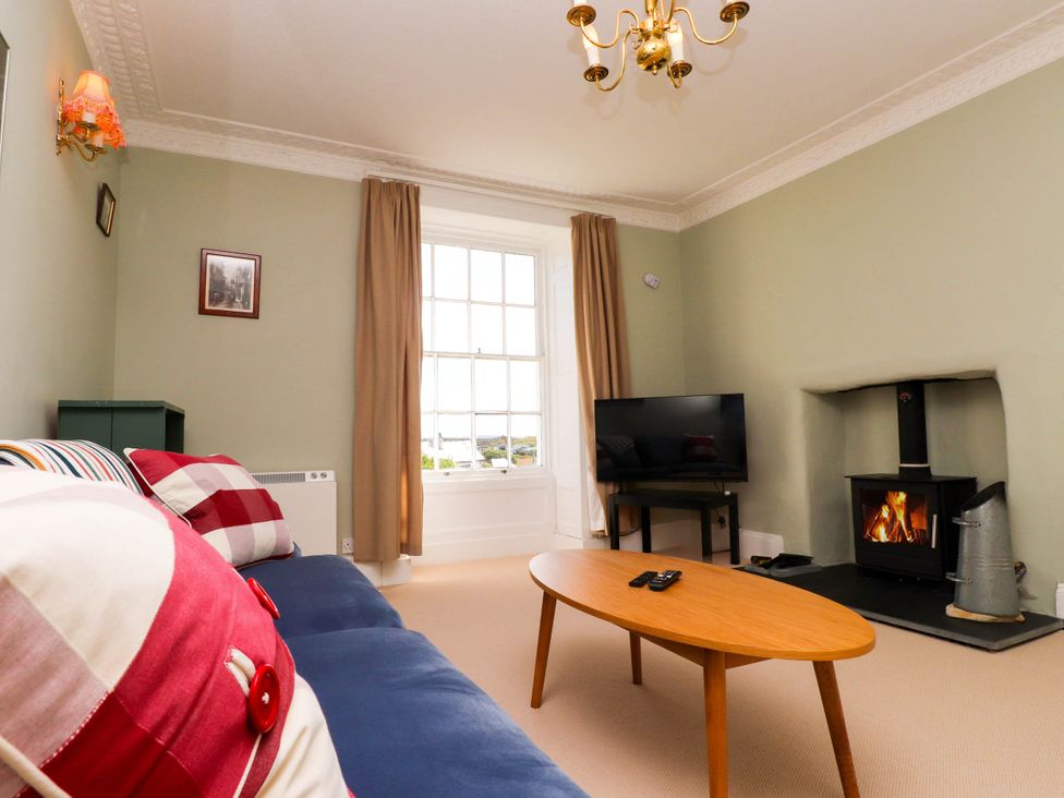 A living room with a blue sofa red and white cushions a wooden coffee table a fireplace and a television at Flat 3 Trearddur Bay