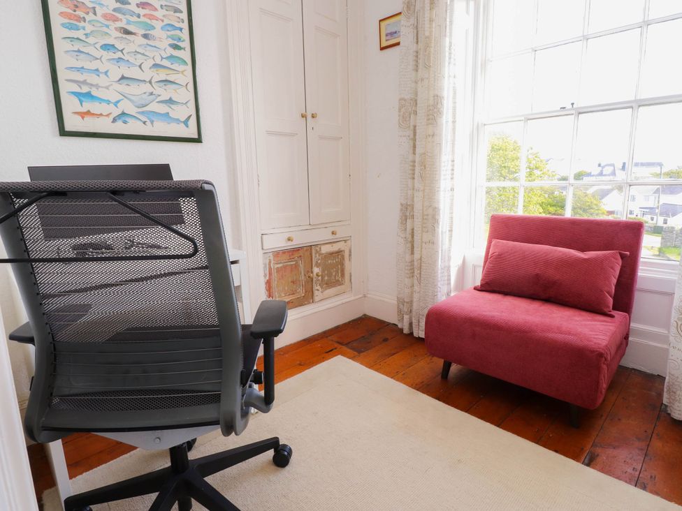 A room with a black office chair a red armchair a framed fish poster and a window with curtains at Flat 3 in Trearddur Bay