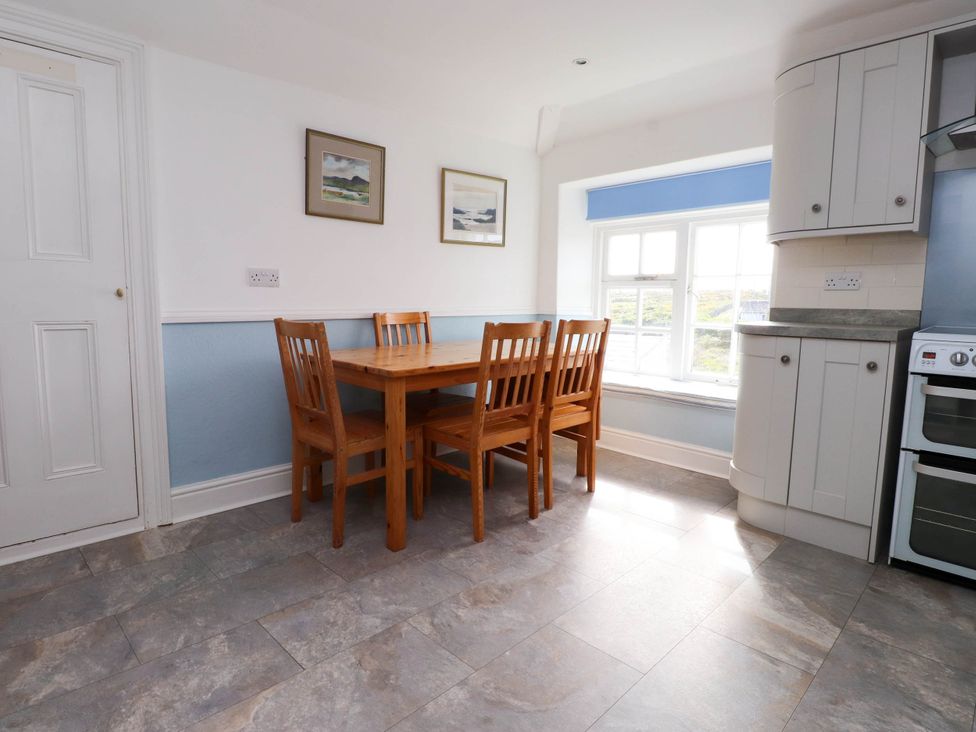 A kitchen dining area with wooden table and chairs near a window and white cabinets at Flat 3 in Trearddur Bay
