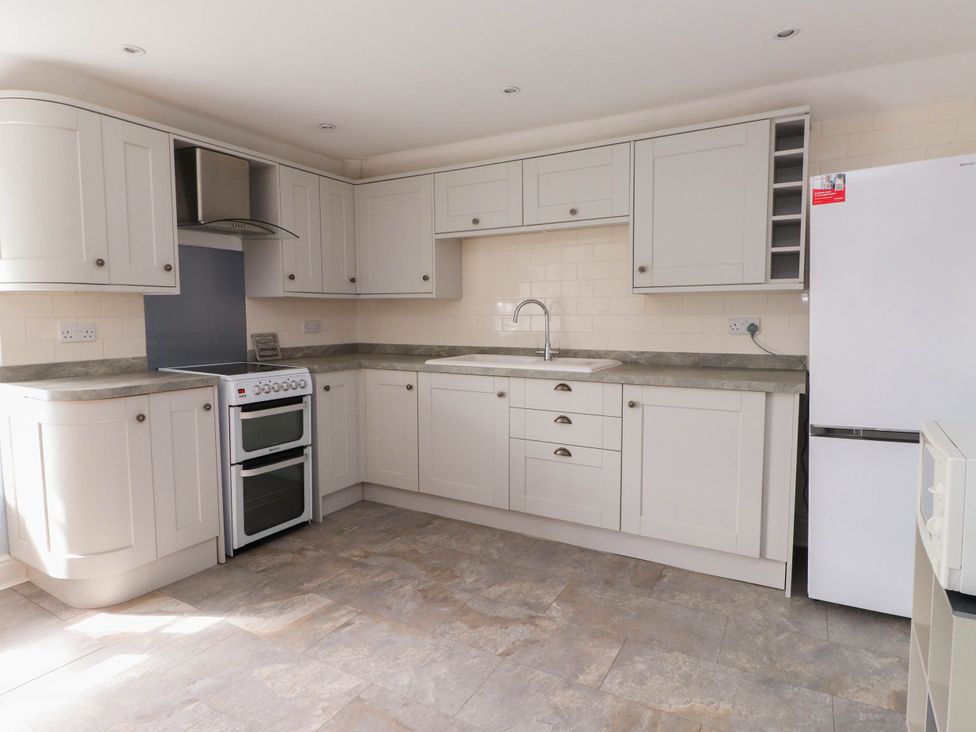 A kitchen with white cabinets a stove a sink a refrigerator and a microwave at Flat 3 in Trearddur Bay