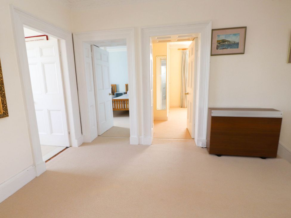 A hallway with beige carpet with three doorways leading to other rooms and a wooden cabinet on the side at Flat 3 Trearddur Bay