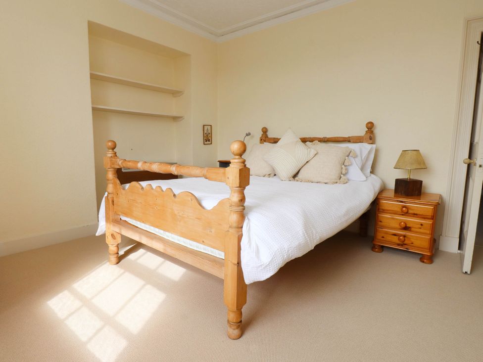 A bedroom with a wooden bed with white bedding a wooden bedside table with a lamp and shelves on the wall at Flat 3 in Trearddur Bay