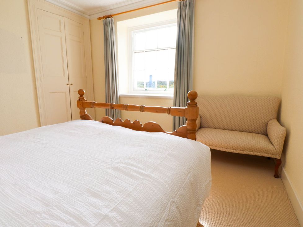 A bedroom with a wooden bed a beige sofa a window with curtains and built in wardrobes at Flat 3 in Trearddur Bay