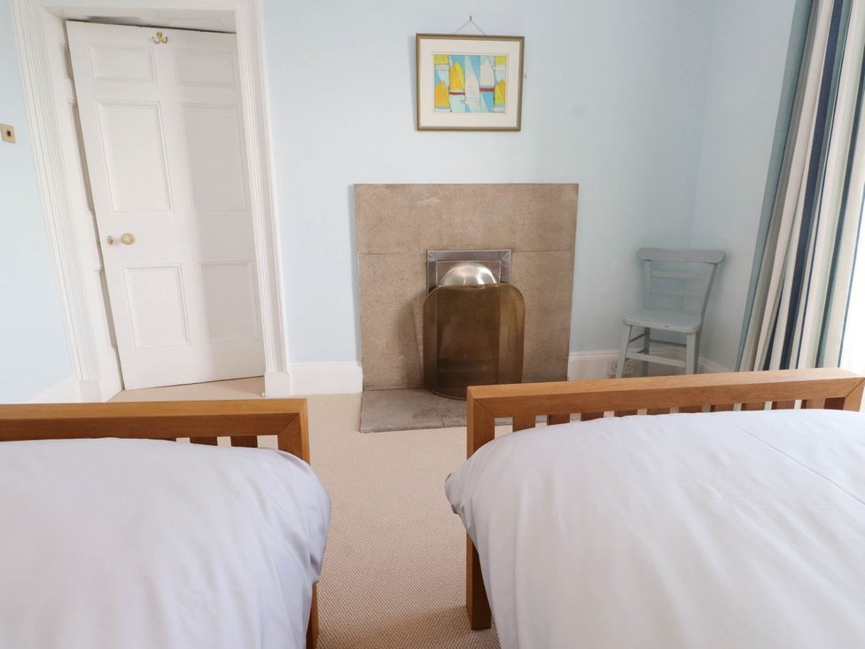 A bedroom with two single beds a fireplace a chair and a door at Flat 3 Trearddur Bay