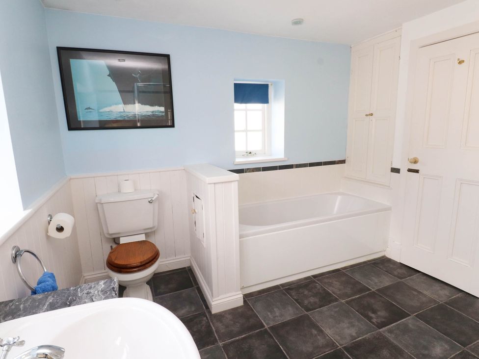 A bathroom with a bathtub toilet a sink a window and cabinets at Flat 3 in Trearddur Bay
