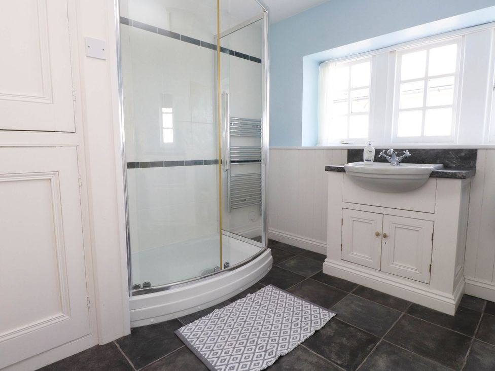 A bathroom with a shower enclosure a sink with cabinet a window and a floor mat at Flat 3 in Trearddur Bay
