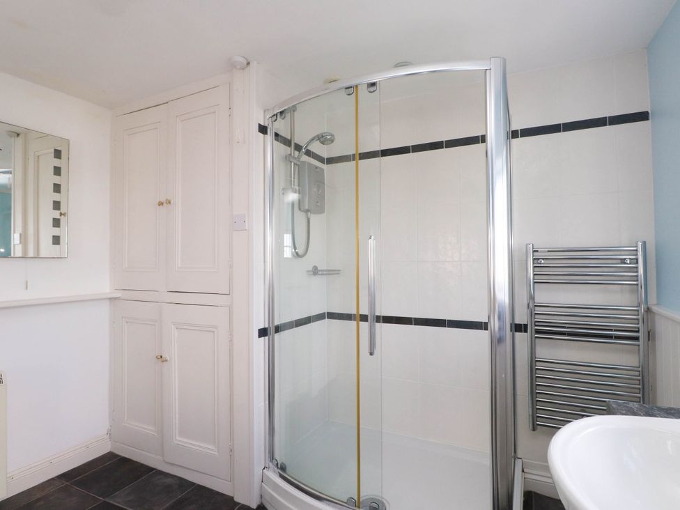 A bathroom with a corner shower enclosure towel radiator storage cupboards and a sink at Flat 3 in Trearddur Bay