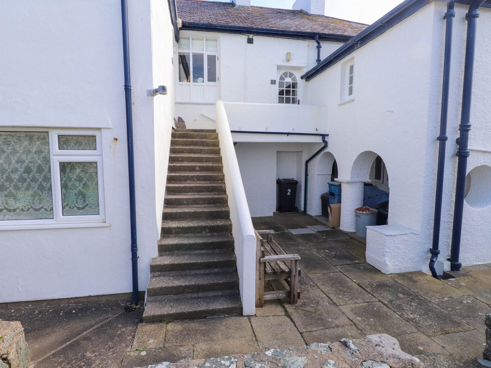 An outdoor area with concrete stairs leading to a white door a wooden bench and various trash bins at Flat 3 Trearddur Bay