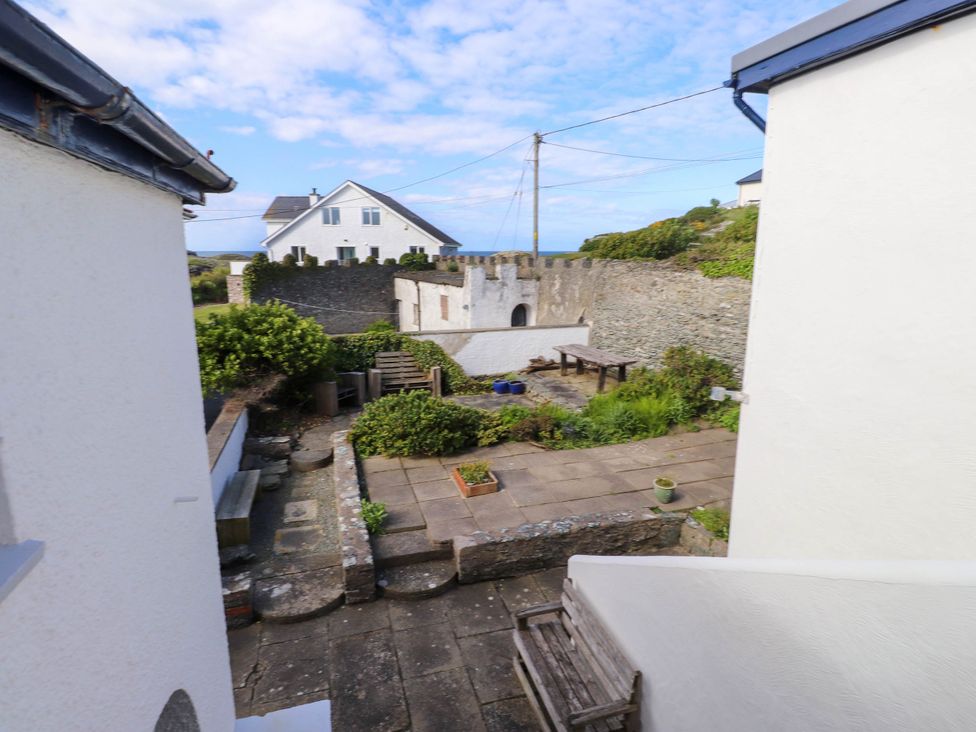 An outdoor patio area with benches tables potted plants stone walls and a white house in the background at Flat 3 Trearddur Bay