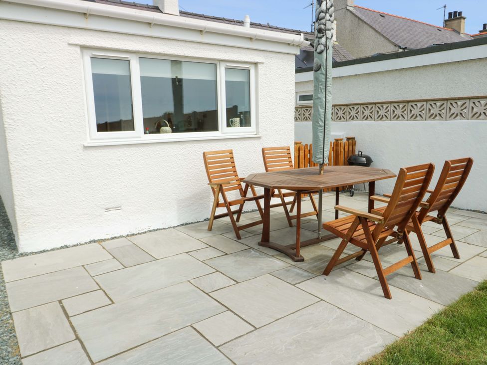 An outdoor patio with a wooden table and four wooden chairs near a white house at Ty Bach in Llanfaelog near Rhosneigr